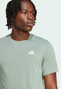 Ljusgrön, kortärmad tränings t-shirt i mjukt material, med en vit Adidas-logotyp på vänster bröst. Rund halsringning.