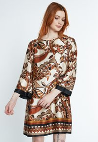 Seidenkleid mit floralen Mustern in warmen Tönen von Braun, Orange und Creme, verziert mit schwarzem Saum an den Manschetten und dem Saum.