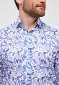 Witte button-up shirt met een blauw paisleypatroon in verschillende tinten blauw en grijs, en een gestructureerde kraag. Soepele stoftextuur.