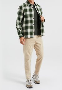 Flannel shirt in green and white check pattern, paired with a dark green top and beige corduroy pants. Gray and tan sneakers.