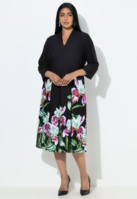 Czarna sukienka z dekoltem w serek i rękawami do łokcia, z kolorowym kwiatowym wzorem przy dolnym brzegu. Materiał wydaje się gładki; dodatkiem są czarne szpilki.
