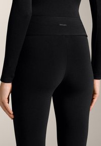 Magas derekú fekete leggings elasztikus anyagból, sima felülettel és diszkrét logóval a derékrészen.