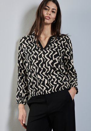 Blusa negra y crema con un patrón geométrico, escote en V y puños elásticos. Tejido suave con un ajuste relajado y dobladillo fruncido.