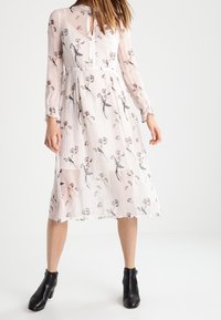 White midi dress with floral print, long sleeves, and a keyhole neckline. Worn with black ankle boots. Lightweight, flowing fabric.