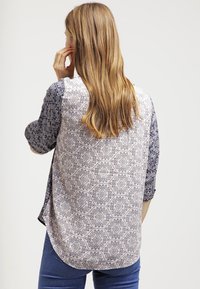 Maglietta a maniche lunghe con schiena a motivi in beige chiaro e accenti blu scuro, caratterizzata da un orlo arrotondato e una texture di tessuto morbida.