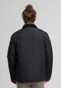 Czarna pikowana kurtka z kołnierzem z kordurowego materiału, luźnym krojem oraz zapięciem na napy przy mankietach. Teksturowany wzór w romby na całej powierzchni.