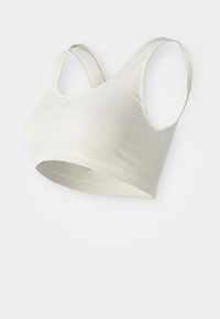 Neprekinjen bež športni modrček z širokimi naramnicami, zaobljenim izrezom in rahlim nagubanjem na sredini spredaj za podporo in udobje.