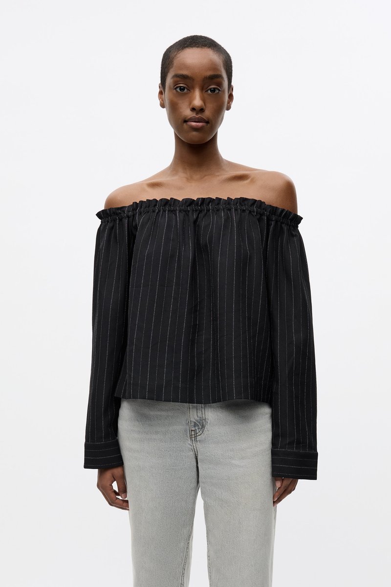 Blusa nera off-the-shoulder con scollo a volant, strisce bianche verticali, maniche lunghe e una vestibilità ampia.