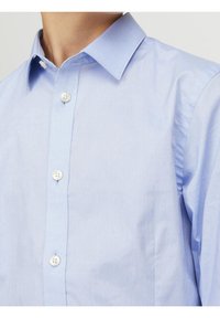 Světle modrá košile s knoflíky vyrobená z bavlny. Má klasický límec, bílé knoflíky a hladkou texturu s jemným leskem.