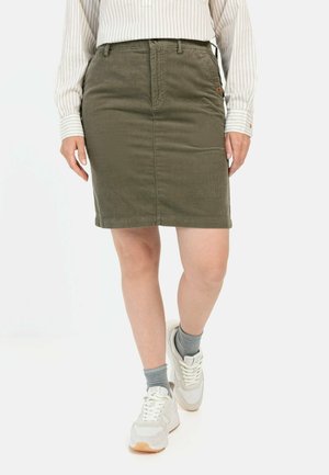 Olivenfarvet kordfløjlsskjørt med en tætsiddende design, forlommer og længde til midten af låret, parret med lyse sneakers og ankelstrømper.