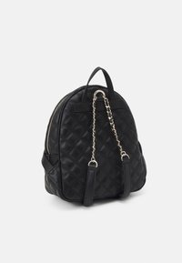 Sac à dos noir matelassé de forme arrondie, doté de quincaillerie en argent, d'une poignée supérieure et de bretelles réglables. Texture lisse avec un design épuré.