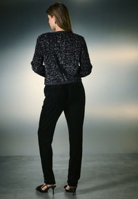 Mustast litritest kaunistatud kampsun ümara kaelusega, mida on kombineeritud mustade sametpükstega ja rihmikute kõrgete kontsadega jalanõudega. Lihtne, sile kujundus.