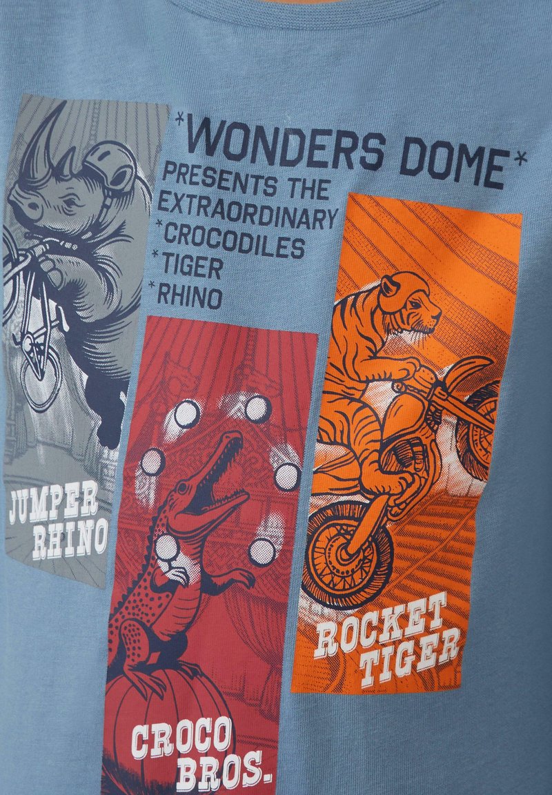Lichtblauw t-shirt met drie grafische panelen met illustraties van een neushoorn, krokodil en tijger, vergezeld van gestileerde tekst.