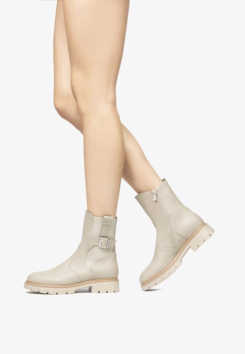 Beige leren enkelboots met een zijrits, gespsluiting en een dikke, gestructureerde zool met opvallende groeven.