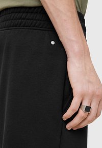 Black jogger pants made of soft fabric, featuring a tapered design, elastic waistband, and a small silver accent near the pocket.
