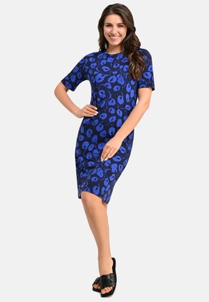 Blaues Kleid mit einem Leopardenmuster, kurzen Ärmeln und einer taillierten Form. Kombiniert mit schwarzen geflochtenen Sandalen.
