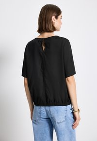 Top corto nero a maniche corte con scollatura rotonda, orlo elastico e dettaglio a chiave sulla schiena. Il tessuto appare liscio con una leggera lucentezza.