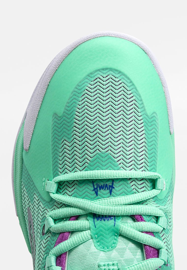 Zapatilla deportiva verde con un upper texturizado, que presenta un patrón en zigzag, acentos en gris y detalles morados en la zona de los cordones.