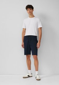 Marineblauwe shorts met een elastische tailleband en trekkoord, gecombineerd met een effen wit T-shirt met korte mouwen en casual sneakers.