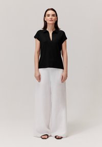 Czarny, krótki top z dekoltem w serek i fakturowanym materiałem, w połączeniu z szerokimi, białymi lnianymi spodniami i czarnymi sandałami.
