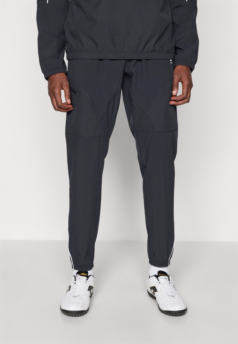 Survêtement de sport gris foncé en tissu léger et lisse ; comporte des poches zippées sur les côtés et des bandes blanches sur les pantalons.