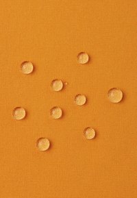 Tissu orange texturé avec plusieurs gouttes d'eau claires reposant sur sa surface, mettant en avant la qualité imperméable du matériau.