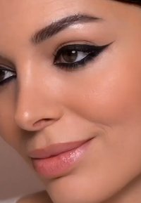 Nahaufnahme eines Gesichts mit glatter Haut, definierten Augenbrauen, einem Flügel-Eyeliner und glänzenden Lippen in einem natürlichen Rosaton.