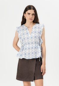 Top peplum bianco con motivo floreale blu, maniche a volants e scollatura a V. Abbinato a una gonna avvolgente marrone. Tessuto liscio, leggero.