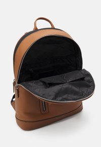 Sac à dos en cuir marron au design arrondi, avec une fermeture éclair et un intérieur noir. Comprend une poche intérieure zippée.