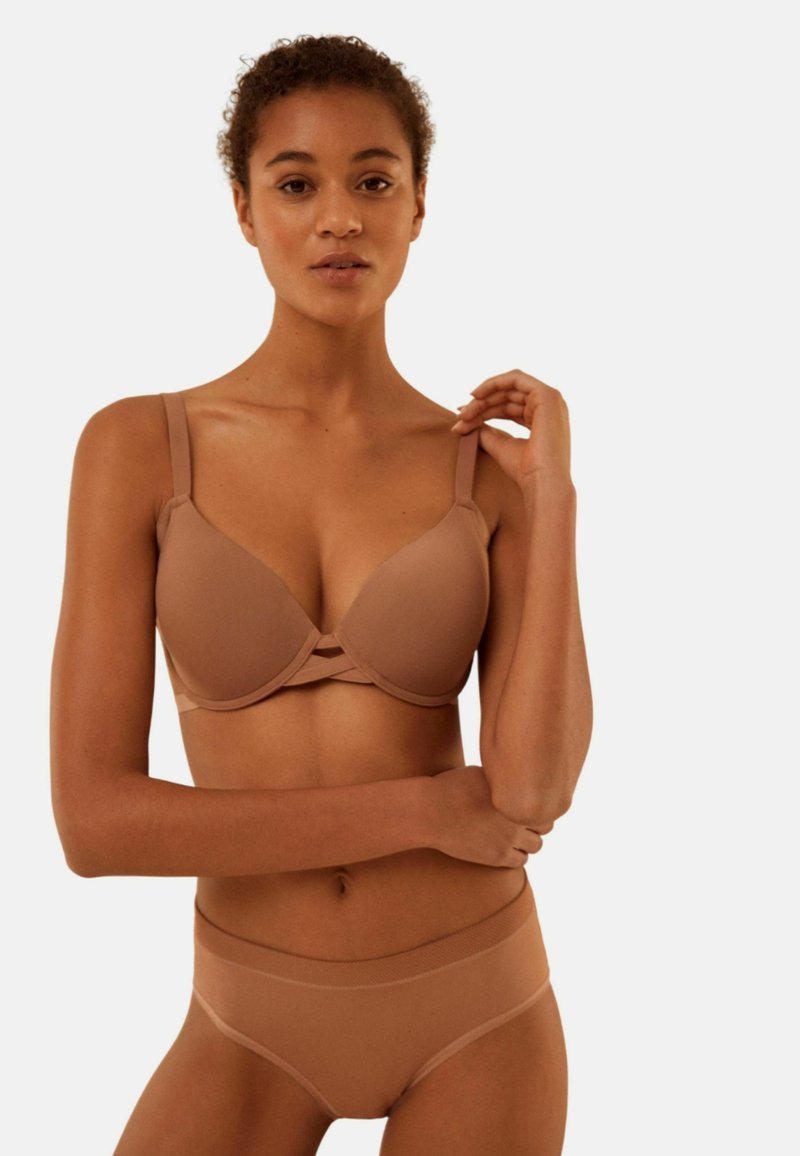Conjunto de sujetador y ropa interior en una tela lisa de color marrón claro. El sujetador cuenta con tirantes ajustables y un escote pronunciado con detalles cruzados.