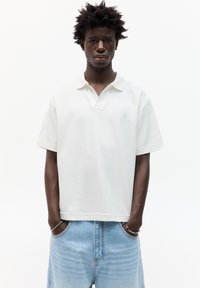 Tricou alb cu guler în V, mâneci scurte și croială lejeră, asociat cu pantaloni şort din denim de un albastru deschis. Textură de material neted.