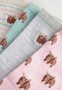 Vier paar gebreide sokken in pastelkleuren: crème met strepen, mintgroen met een hooglandkoe ontwerp, grijs met paarse strepen en roze met koeien.