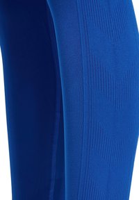 Close-up van blauwe getextureerde leggings met geometrische geribbelde patronen langs het been.