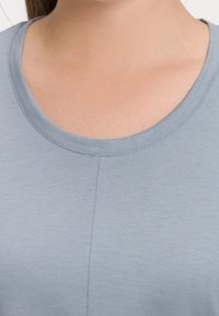 Ljusblå t-shirt med rund halsringning, kortärmar och en slät, mjuk textur. Synlig söm längs mitten fram.