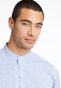 Camicia azzurro chiaro con colletto cinese, realizzata in tessuto testurizzato con leggere sfumature più scure in tutto il capo.