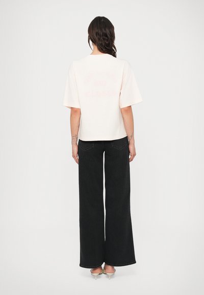 Light pink short-sleeve t-shirt with a cropped design, featuring "CLOSED" printed in a faded style on the back. Paired with wide-leg black trousers.