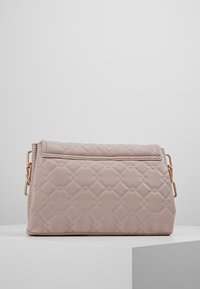 Quiltet lyserød håndtaske med gyldent hardware, der har en fold-over klap og en diagonal lynlåsdetalje, der viser en glat tekstur og en struktureret form.