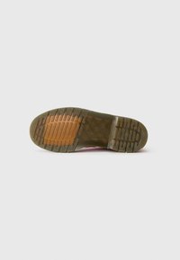 La semelle de la chaussure présente un caoutchouc marron texturé avec des rainures pour une meilleure adhérence, des accents vert clair, et une section translucide claire.
