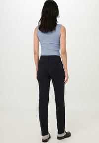 Obtažený modrý bezrukávový top, spárovaný s tmavě námořnickými slim-fit kalhotami s zadními kapsami a čistou, hladkou texturou. Žádné nápadné vzory.