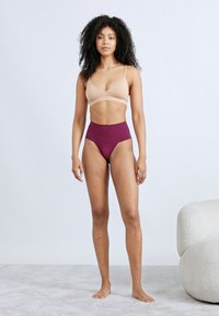 Μπεζ σουτιέν με λεπτές τιράντες συνδυασμένο με ψηλόμεσο, βυσσινί σλιπ. Λείο υφής, μίνιμαλ σχεδιασμός και χωρίς ορατές διακοσμήσεις.