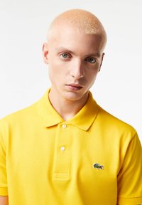 Polo giallo realizzato in tessuto texturizzato, con colletto classico, due bottoni e logo coccodrillo verde Lacoste sul lato sinistro del petto.