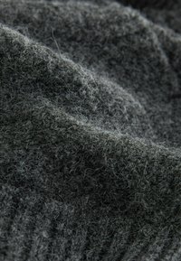 Strukturiertes graues Strickmaterial, das weiche, flauschige Fasern mit einem wellenförmigen Muster aufweist und unterschiedliche Dicken sowie zarte Garne zeigt.