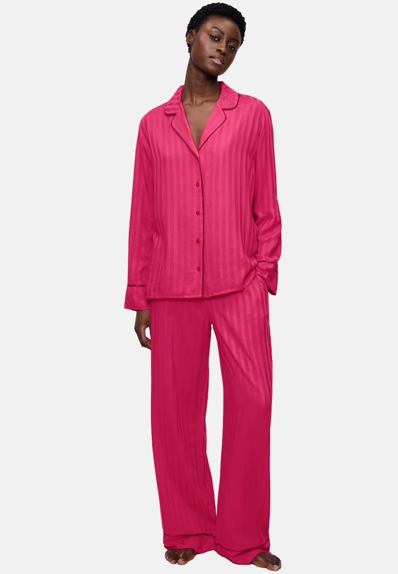 Rosa satinpajamaset med en collared button-up skjorta med ränder och matchande vida byxor, båda med en slät textur.