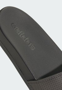 Zwarte Adidas slide met een gestructureerde bovenzijde met perforatie-details en een geperst logo; platte zool met een gladde afwerking.