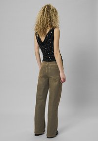 Czarny top bez rękawów z dekoltem w kształcie czołówki i rozrzuconymi białymi kropkami, w połączeniu z brązowymi spodniami o wysokim stanie i szerokich nogawkach.