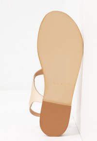 Nude-sandaalit, joissa on litteä ruskea pohja ja pehmeä tekstuuri. Kengässä on yksi hihna ja siinä lukee "Valmistettu Italiassa", koko 37.