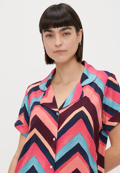 Košulja kratkih rukava od lagane tkanine koja ima chevron uzorak s naizmjeničnim bojama ružičaste, plave i tamnocrvene. Dizajn s gumbima sprijeda.