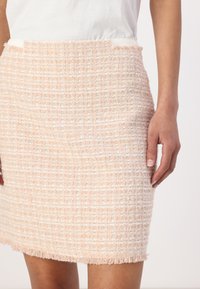 Saia de tweed rosa com um padrão texturizado, bainha desfiada e um design ajustado. O tecido apresenta uma trama quadriculada com sutis acentos brancos.
