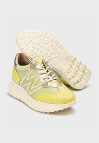 Zapatilla verde lima y dorado metálico con parte superior de malla, lengüeta acolchada y suela de goma blanca texturizada que presenta un patrón de puntos en relieve.