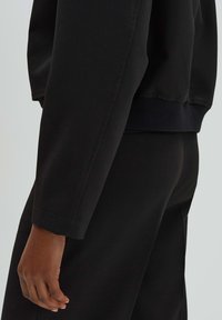 Zwarte sweatshirt met lange mouwen. Gemaakt van gladde stof, met ribgebreide manchetten en een comfortabele pasvorm. Subtiele stikdetails langs de naden.